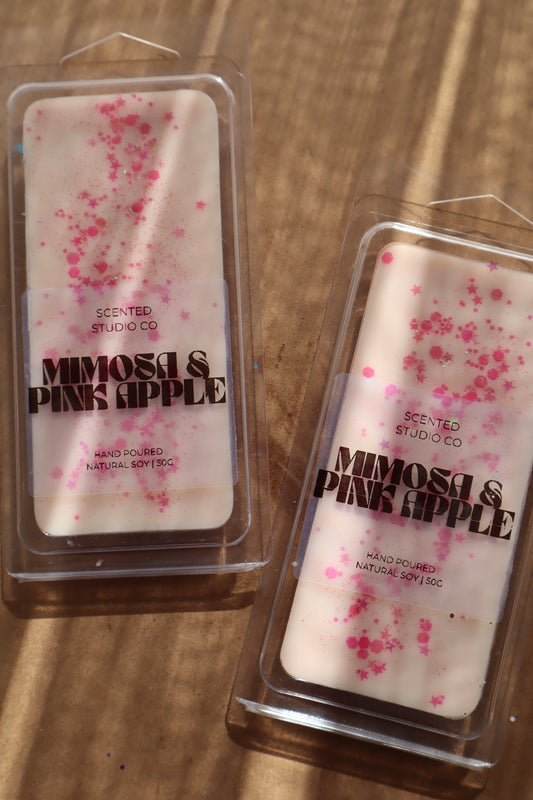 Two scented wax melts in packaging labeled 'Mimosa & Pink Apple' on a wooden surface.